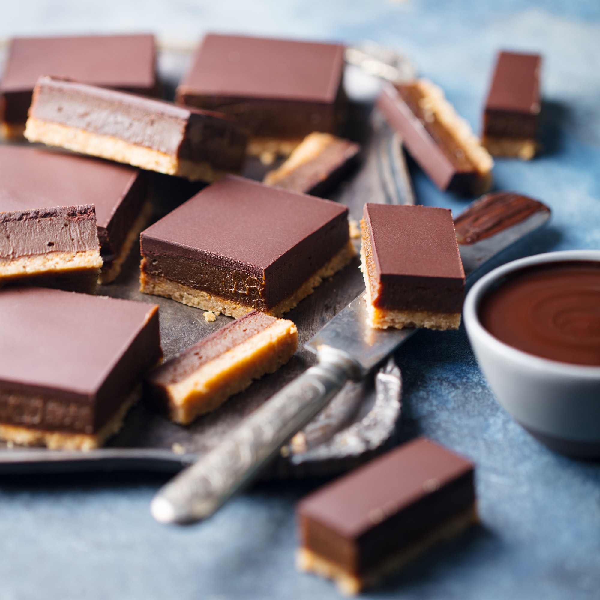 Chocolate Caramel Slices, Bars, Millionaires Shortbread on a Metal Tray. Blue Background.