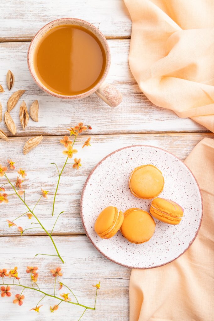 Orange macarons or macaroons cakes with cup of apricot juice on a white wooden background