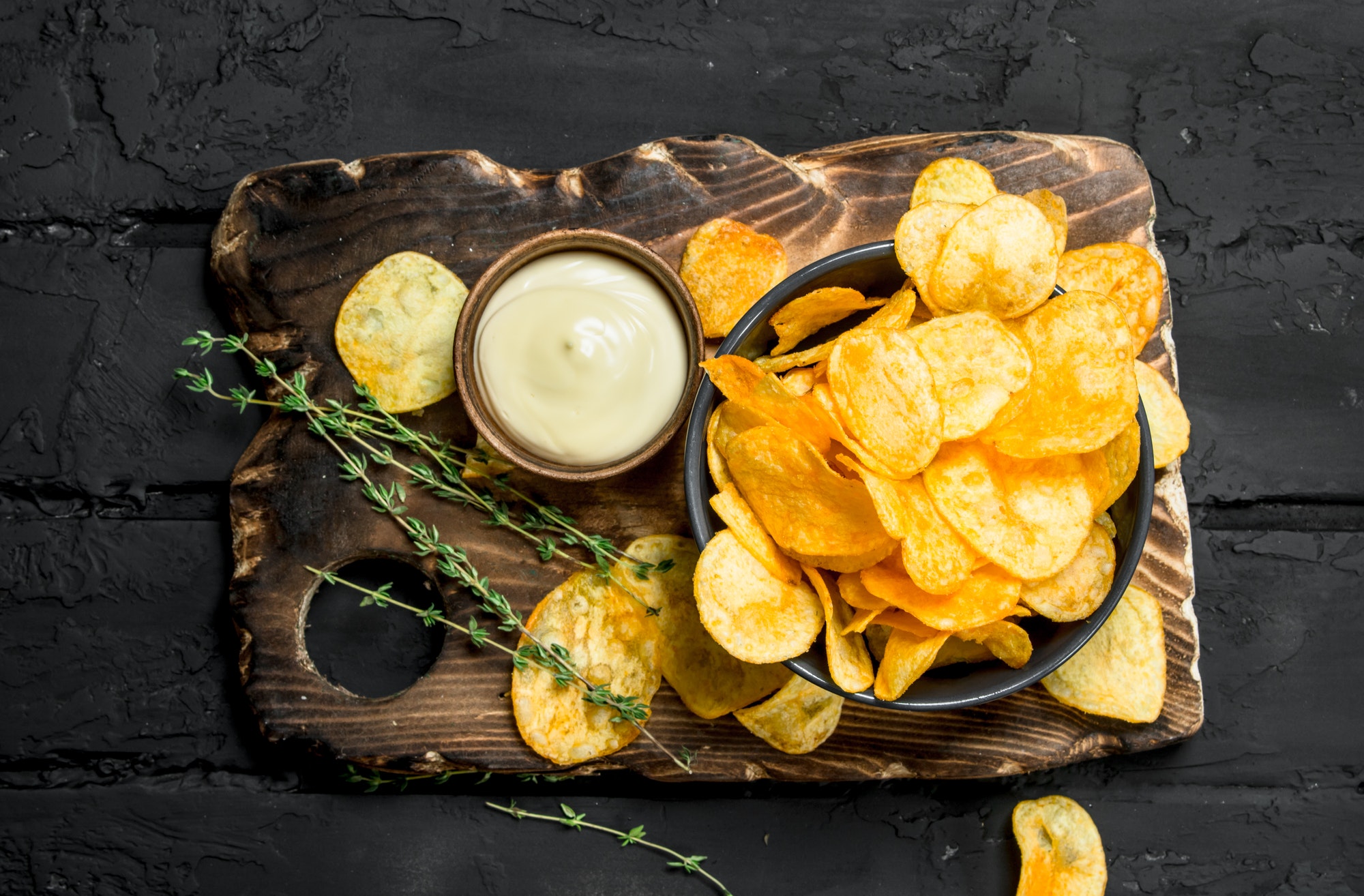 Potato chips in bowl with sauce and thyme.