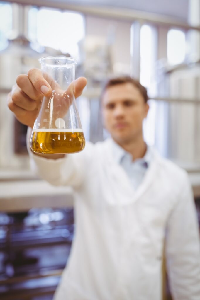 Thoughtful scientist holding a beaker in the factory
